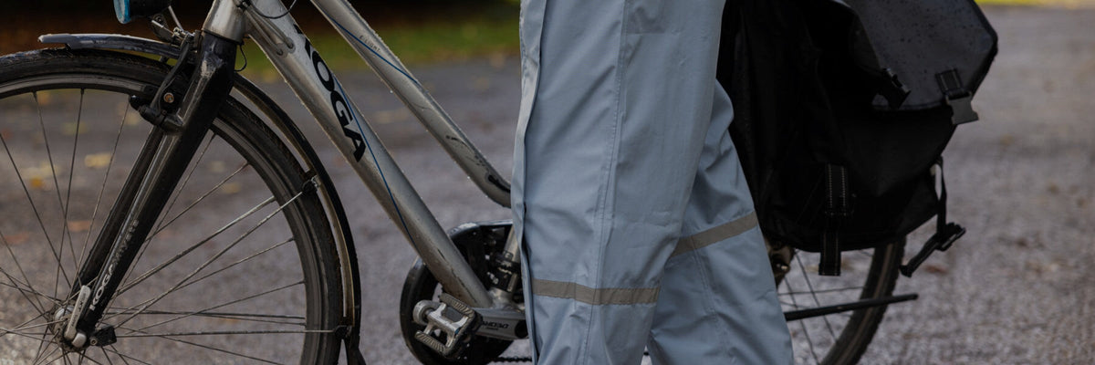 Cycliste en pantalon de pluie Hello Rain bleu clair à côté de son vélo