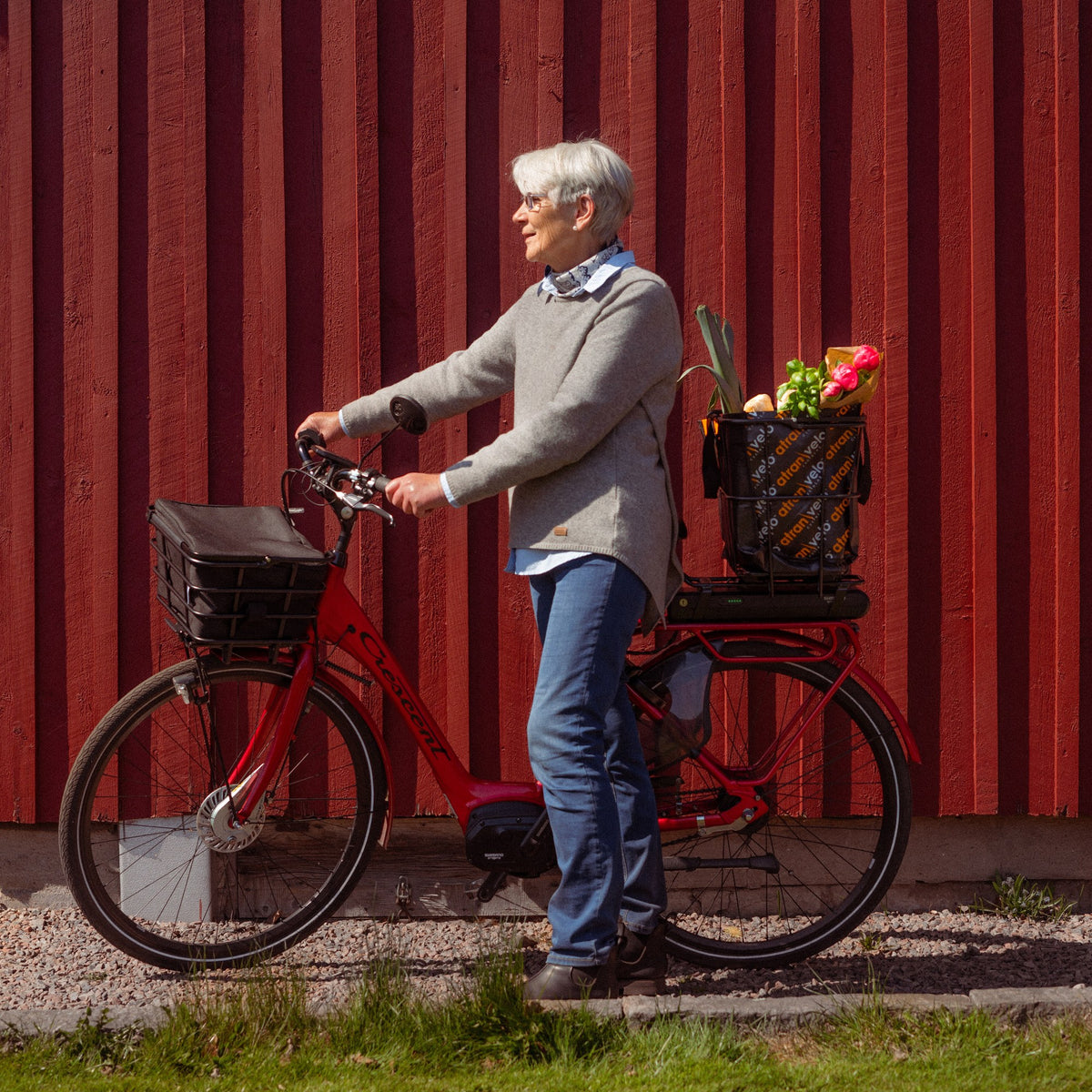 Cycliste avec un vélo électrique équipé de paniers AtranVelo devant une façade rouge