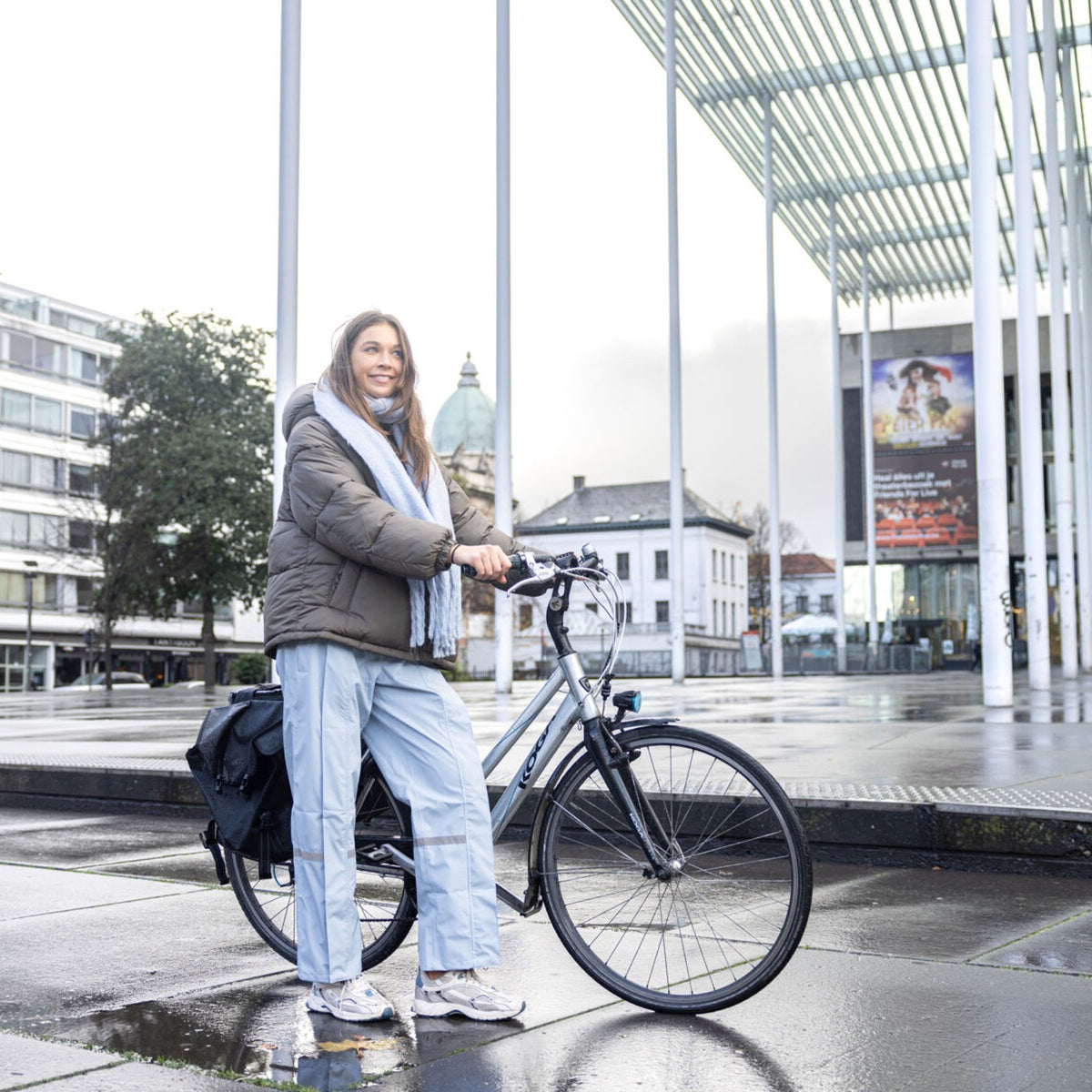 Cycliste en pantalon de pluie Hello Rain sur une place mouillée