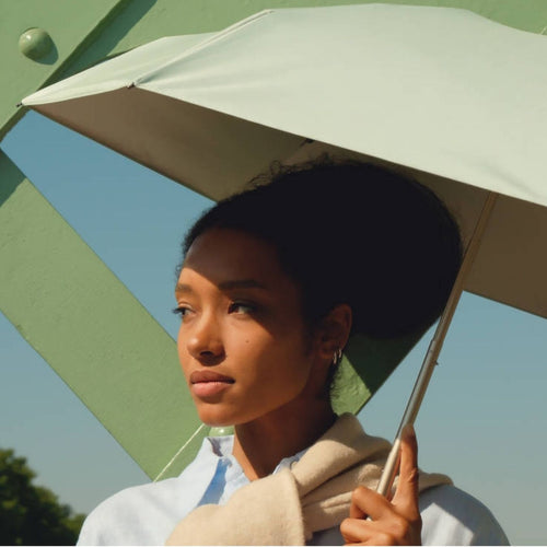 Parapluie-ombrelle anti-UV Anatole vert lagon porté sur un pont en ville